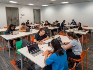 Students in a classroom at City College Perth, engaged in group activity, using laptops and books,